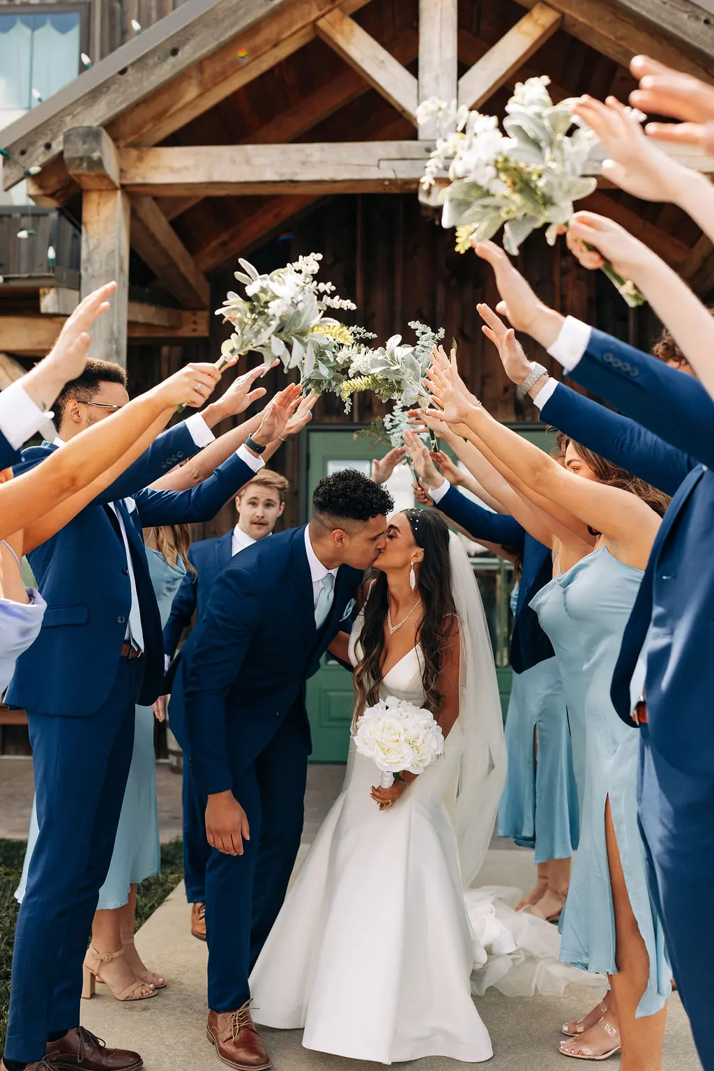 453 the bakers say i do at the pearl Bride and groom kissing under an arch of raised arms and floral bouquets, celebrating their wedding at The Pearl, a picturesque venue in Missouri.