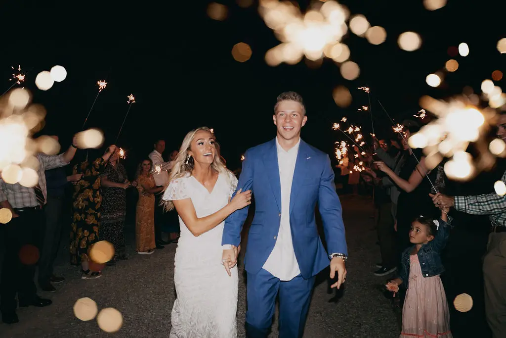 86 sarah and tyler at our kansas city wedding barn Bride and groom joyfully exiting their wedding reception, surrounded by guests holding sparklers, celebrating their special day at The Pearl at Crawford Farm.