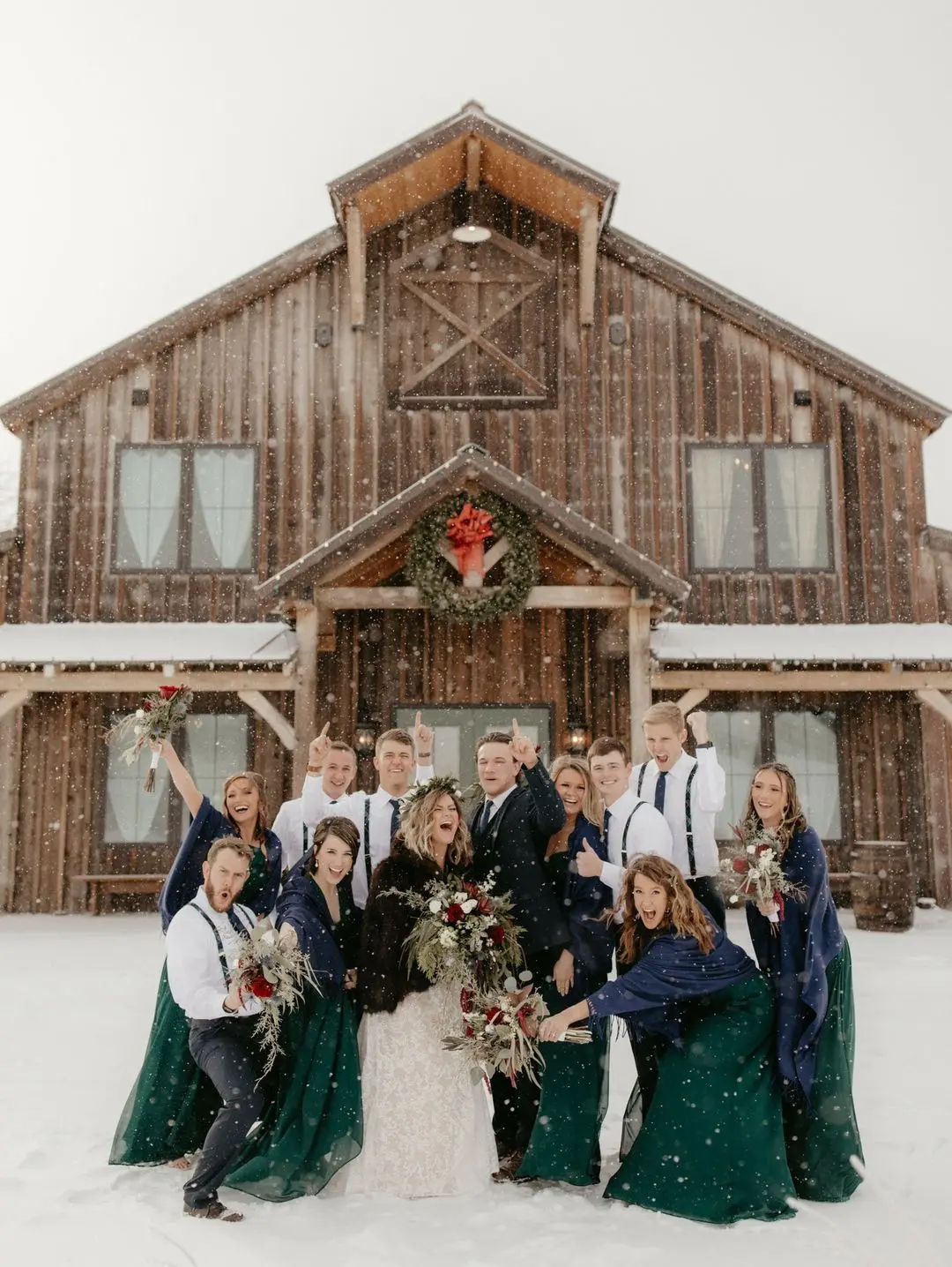 Wedding couple and bridal party celebrating in front of The Pearl barn venue, adorned with a holiday wreath, surrounded by snow during a winter wedding.