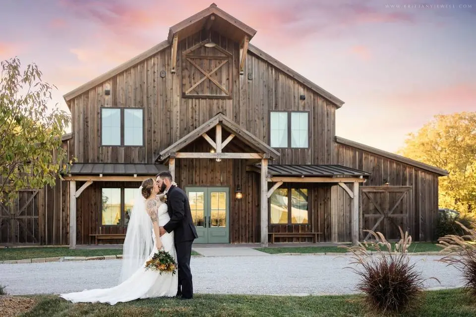 couple wiht a gorgeous pink sky at the pearl Couple embracing in front of The Pearl at Crawford Farm, a rustic wedding venue with wooden exterior and vibrant pink sky, symbolizing a romantic wedding setting.