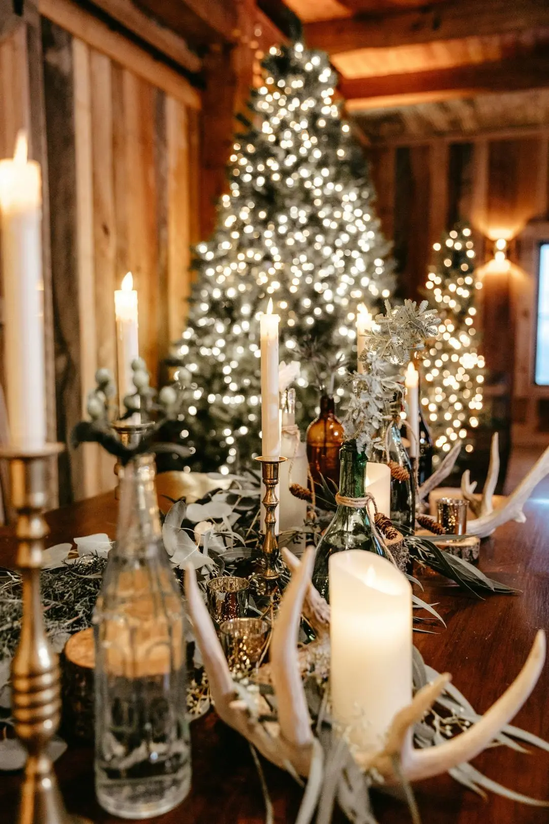 gorgeous christmas tree and decor Christmas-themed table setting with candles, greenery, and decorative antlers, featuring a beautifully lit Christmas tree in a rustic wedding venue, ideal for winter weddings at The Pearl at Crawford Farm near Savannah, MO.