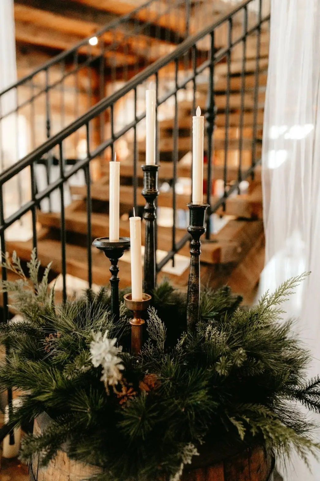 gorgeous gardland and winter candles Candle centerpiece with winter greenery, rustic decor elements, and wooden staircase in a wedding venue setting at The Pearl at Crawford Farm.