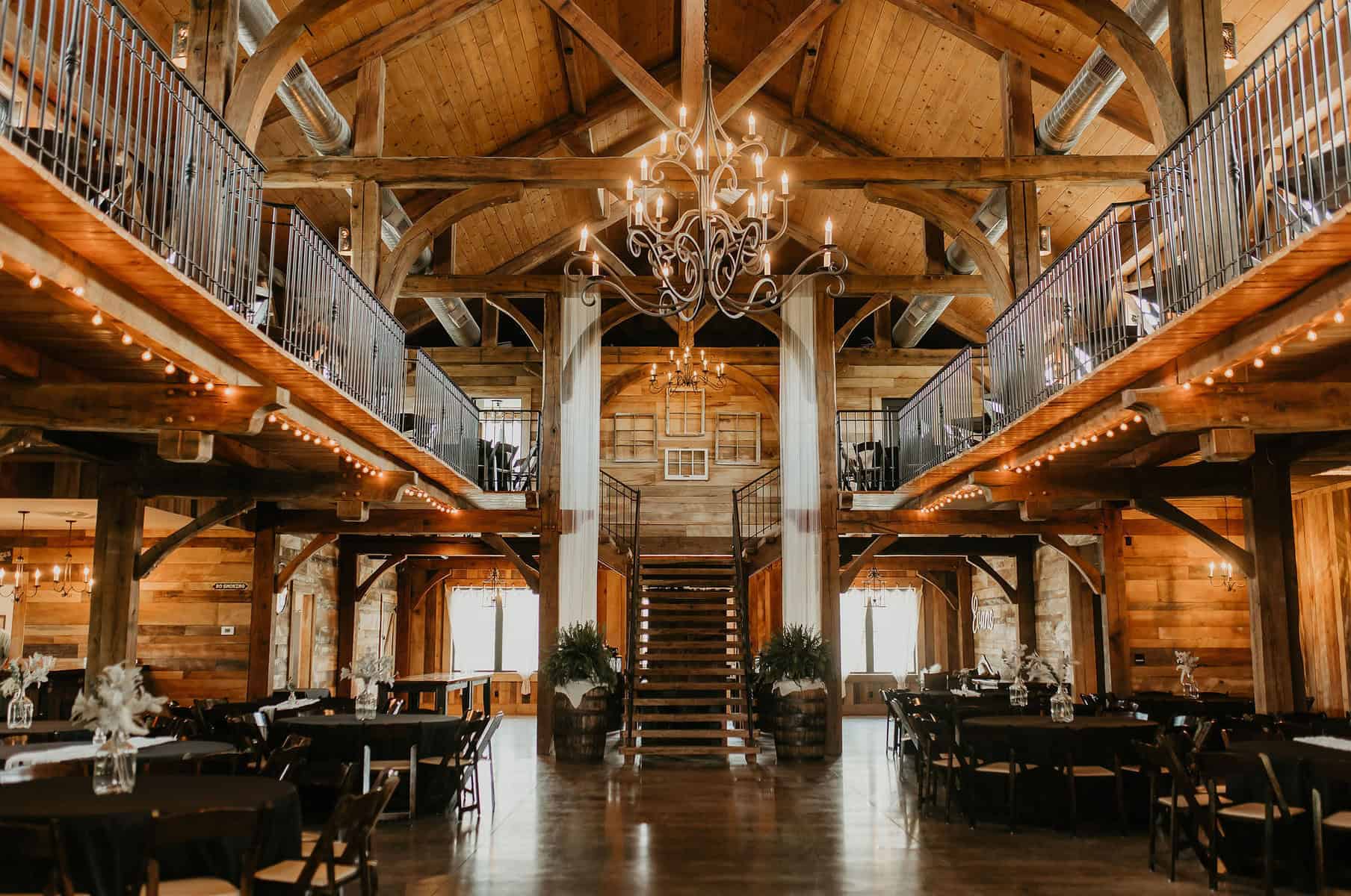 missouri wedding barn the pearl at crawford farm Interior of The Pearl at Crawford Farm, showcasing wooden beams, elegant chandeliers, and a spacious layout with dining tables, ideal for weddings in St. Joseph, MO.