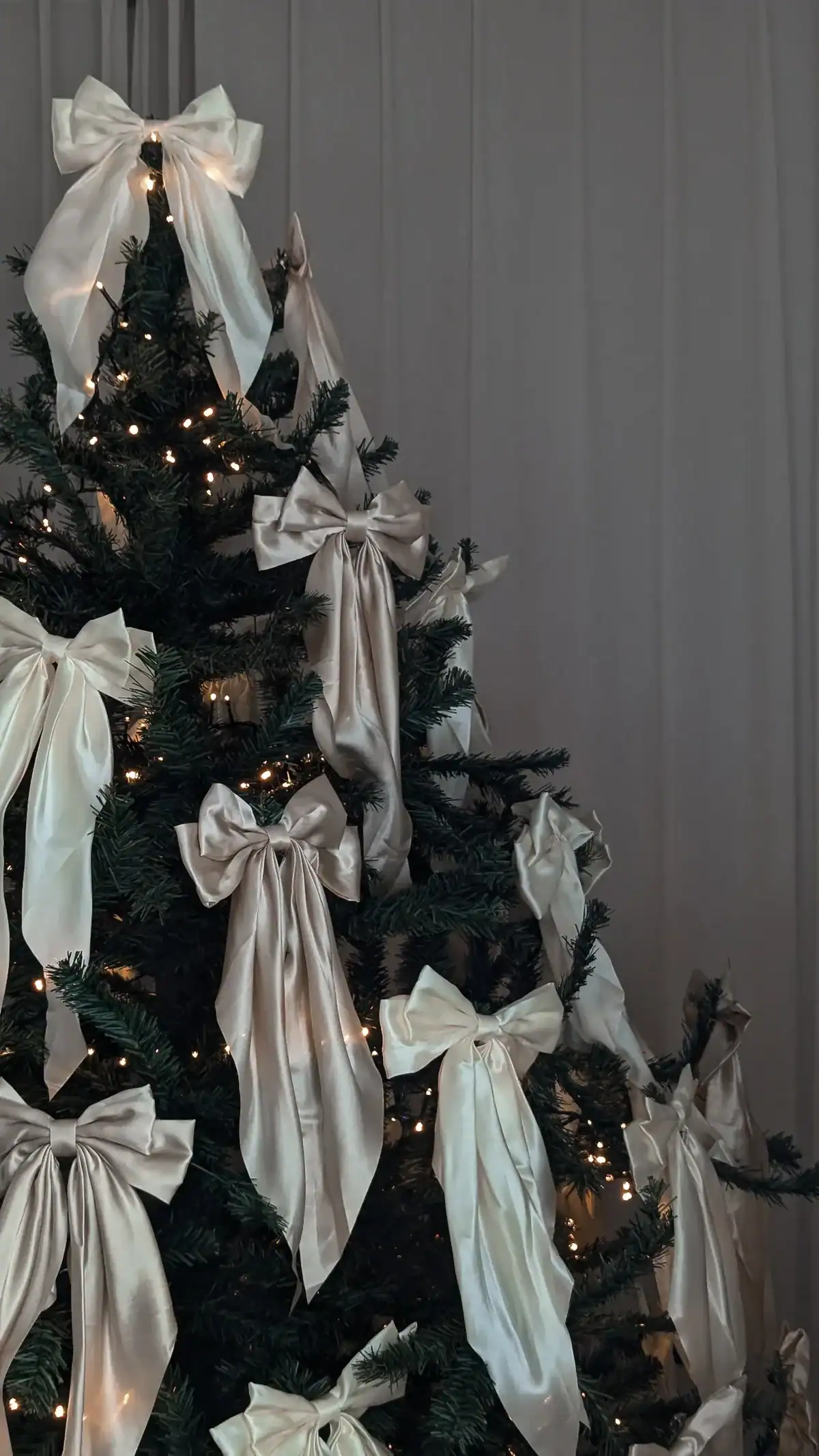 Christmas tree adorned with elegant cream-colored satin bows and warm fairy lights, enhancing a cozy winter wedding atmosphere.