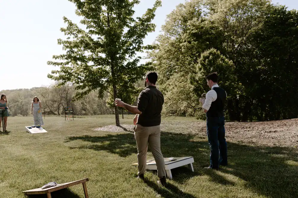 Group of friends playing outdoor lawn games at a wedding venue in Topeka, surrounded by greenery and trees, showcasing a relaxed and festive atmosphere.